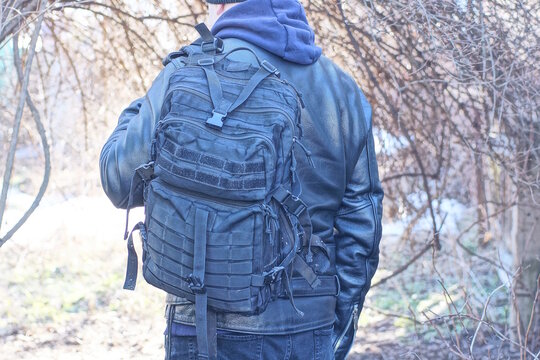 one black army backpack on the back of a man and leather jacket on an autumn street