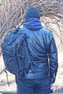 one black army backpack on the back of a man and leather jacket on an autumn street