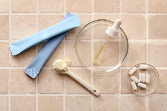 Collagen jelly sticks, pills, pipette and teaspoon of powder on beige tile background
