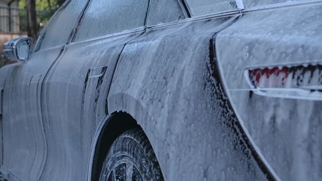 Close up shot of foamy water sliding down dark colored car during washing process