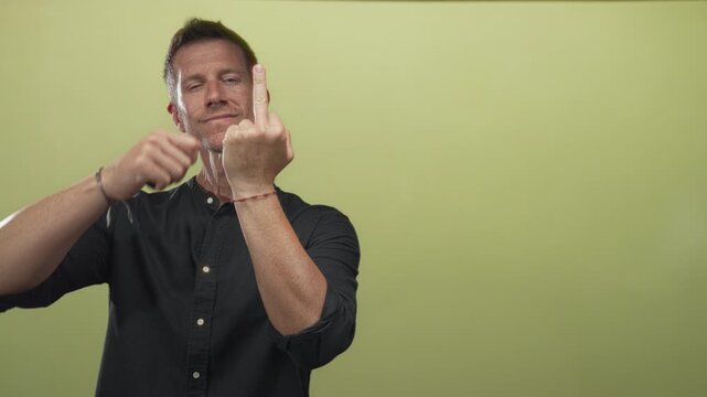 Man showing middle finger and bare hand wearing bracelet in lime green studio, direct stare and raised forearm; defiance.