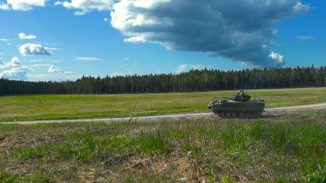 Armored vehicle drives down a dirt road near forest and open field