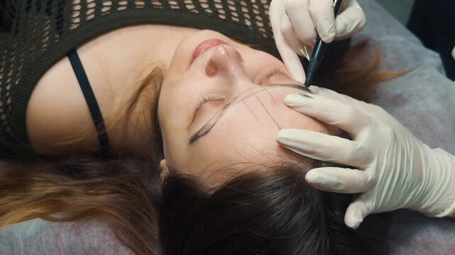 Woman client undergoing an eyebrow mapping procedure for permanent makeup. With a beautician carefully marking the perfect shape on her face. Ensuring precision before a microblading beauty treatment