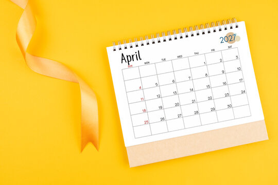 April 2027 desk calendar with yellow ribbon on yellow color background.