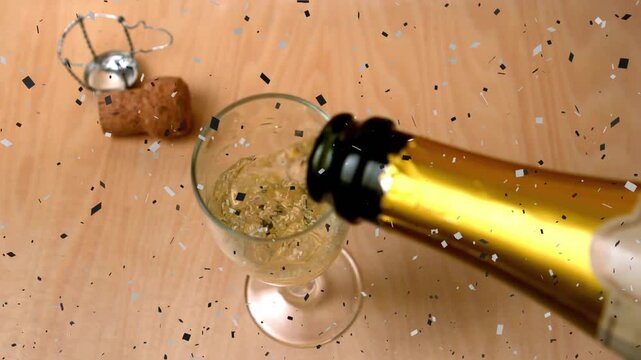 Opened gold-foil bottle pouring golden bubbles into stem glass, filling slowly with confetti