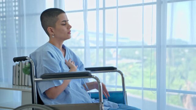 Female patient sitting in wheelchair experiencing chest discomfort inside hospital room, medical emergency and healthcare concept