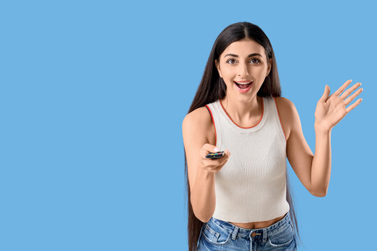 Happy young woman with remote controller on blue background