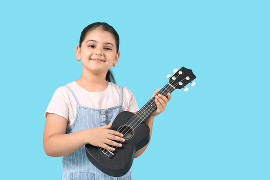 Little girl playing ukulele on blue background