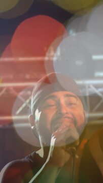 Vertical video: Focus pull revealing male singer holding mic, singing with bokeh overlays for music
