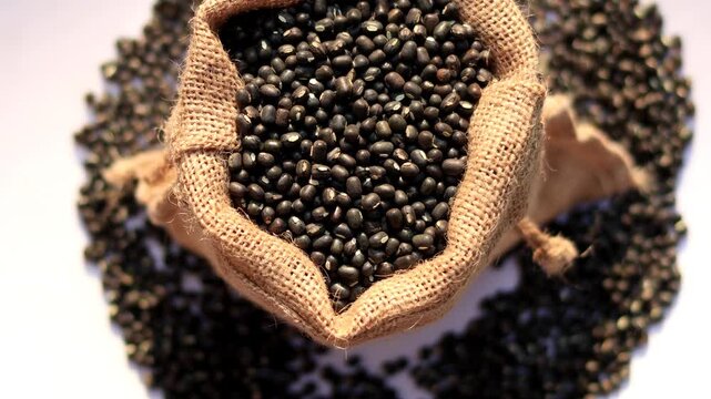 Black Lentil/ masoor dal filled in jute sack table top spin isolated on white background.