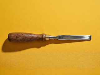 Obraz premium Minimalist Woodworking Chisel Photograph Polished Steel Walnut Handle Mustard Background