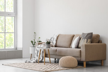 Naklejka premium Interior of light living room with grey sofa, table and pouf