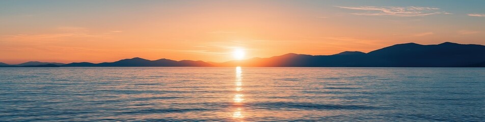 Fototapeta premium Sun setting behind distant mountains, reflecting orange light on the calm ocean surface. Serene nature scene at twilight