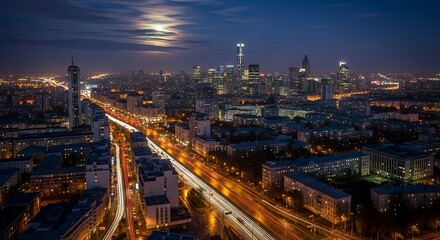 Fototapeta premium Aerial view of a city at night. Car light trails and moon glow. Buildings and illuminated roads