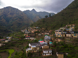 Fototapeta premium Stunning aerial view of a remote mountain village nestled in the hills, surrounded by beautifully layered terraced fields. The warm golden sunlight highlights the natural contours of the landscape.