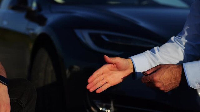 Male hand giving key of car to buyer of electric automobile outdoor. Handshake between salesman and new owner of modern auto after successful deal. Concept of buy or rent car. Slow mo