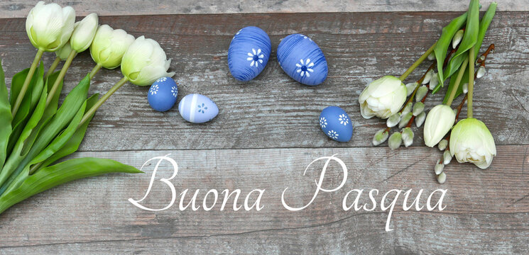 Fiori e uova di Pasqua dipinte di blu su uno sfondo di legno con la scritta in italiano 'Buona Pasqua'