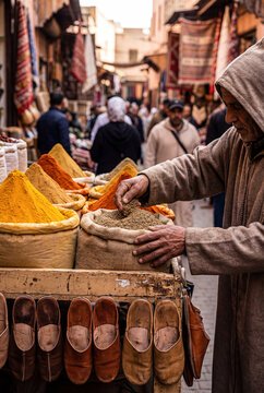 Moroccan spice market with merchant in traditional clothes, oriental bazaar with colorful seasonings and leather shoes.