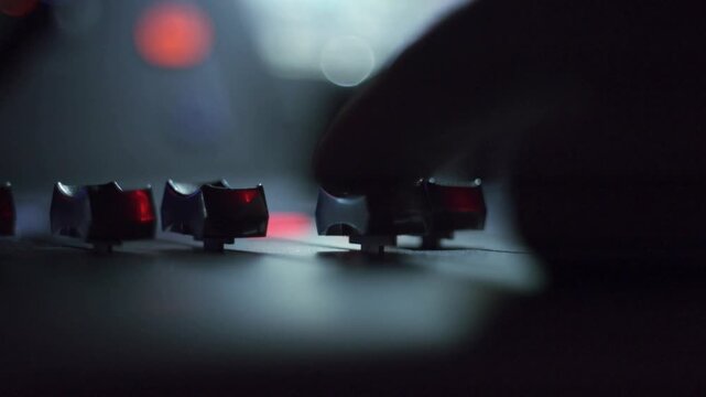 Closeup of audio mixer controls with a hand adjusting a fader in a dimly lit studio