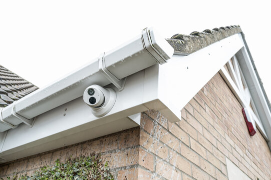Newly installed WiFi dome night and day CCTV camera installed under plastic guttering in a private house in Britain. An alarm siren box can just be seen on the right, below the roof apex.