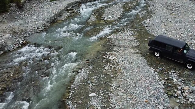 Aerial shot of an off-road vehicle crossing a rocky river stream, metaphor for navigating through change, resilience, and successful transition. Kyrgyzstan, Karakol