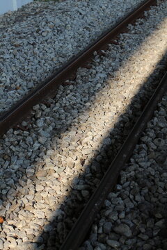 Sunlight streams across weathered railroad tracks and gravel ballast