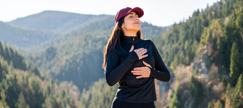 Relaxed woman breathing fresh air in a green pine forest and making breathing exercises 