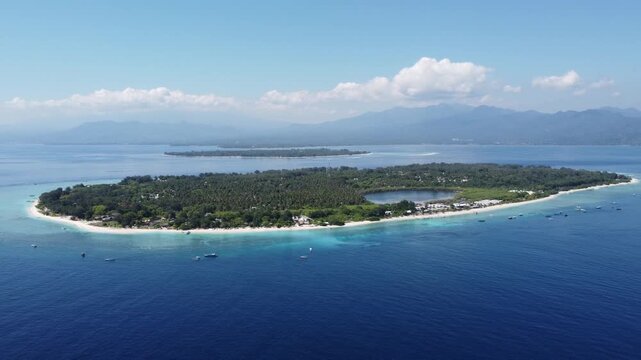 Aerial drone orbiting left at high altitude above Gili Trawangan with Gili Meno and Lombok behind, Indonesia.