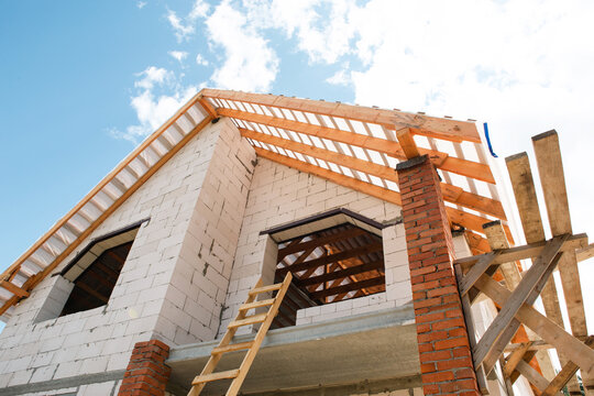 Modern block house with wooden roof lags and trusses, active phase of mounting roof structure, light finished bricks.
