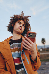 A young woman with curly hair wearing a striped rainbow sweater and orange jacket holds a...