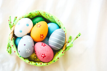 Fototapeta premium Colorful eggs in a small basket on a light background during spring celebration of Easter holidays