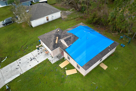Hurricane Ian damaged house rooftop covered with protective plastic tarp against rain water leaking until replacement of asphalt shingles. Aftermath of natural disaster