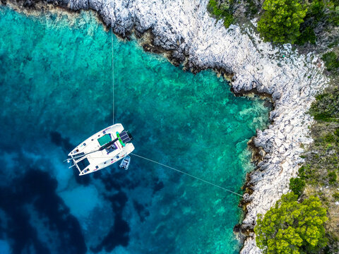 Aerial top-down view of catamaran moored stern-to rocky limestone coastline with turquoise water, &Scaron;ćedro Island, Hvar, Croatia