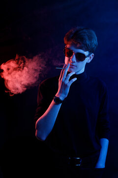 Handsome man in dark outfit smoking, dramatic  and cinematic aesthetic with vibrant red and blue neon lighting.