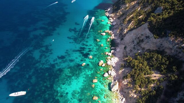 Sardinia Coastline Drone Video, Flying Along Massive Cliffs with Boulders over Transparent Water, Aerial View Tilting Up to Cala Goloritze on Horizon with Speeding Motorboats, Orosei Gulf 4K Cinematic