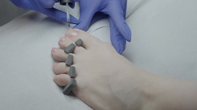 Polish application on toes using precise brush and toe separators, glossy finish applied by gloved technician, careful drying