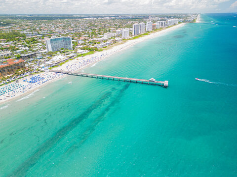 Aerial view of a South Florida coastline with high-rise condominium buildings and pier extending into the ocean. 