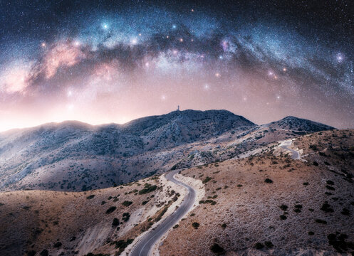 Milky Way arch and winding mountain road at night. Sky with arched milky way and bright stars in summer. Lefkada, Greece. Top view of empty road, hills. Beautiful landscape with highway, space. Travel