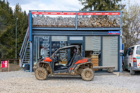 Zakopane, Lesser Poland, Poland - March 22, 2026: A mud-splattered orange Can-Am Maverick buggy stands parked before a modern outdoor adventure rental hub.