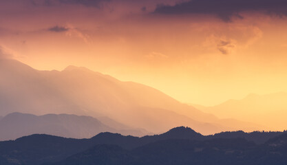 Naklejka premium Silhouettes of Alpine mountains at colorful sunset in summer in Slovenia. Landscape with mountain ridges in fog, golden sunlight and clouds in the evening. Alps. Nature. Hills in sunlight. Scenery