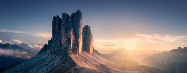 Naklejka premium Epic rocky mountains at sunset in autumn in Dolomites, Italy. Colorful landscape with alpine mountains, orange grass on the hill, golden sky in fall. Aerial view of high rocks. Tre Cime park. Alps