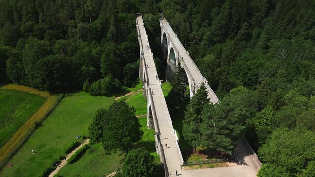 Aerial Orbital Shot of Historic Stańczyki Viaducts in Poland - Twin Stone Arched Bridges Surrounded by Lush Green Forest