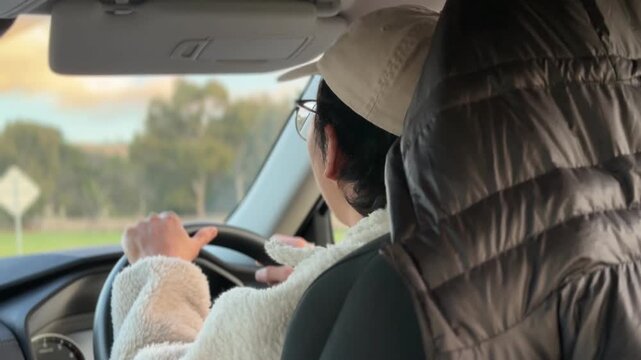A man wearing glasses driving a car on an open Australian highway surrounded by dry grassland