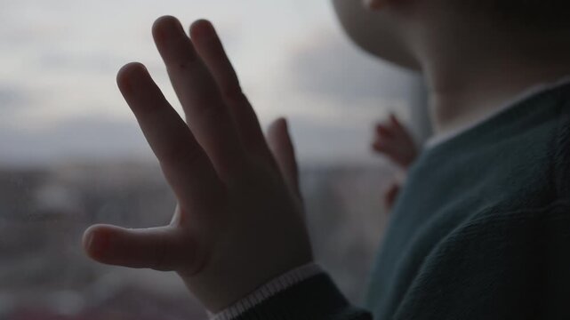 Toddler boy looking out of the window with hands on glass, cinematic video