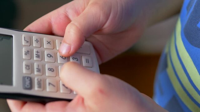Child's Hands Pressing Buttons on White Desktop Calculator Close-Up &mdash; Boy Using Calculator, Maths Learning, Numeracy and Early Education Concept