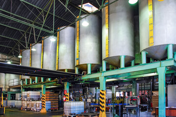 Industrial facility featuring large on a green metal structure, with IBC totes, barrels, and equipment below in a warehouse setting. Focused on chemical or oil processing. © lcrribeiro33@gmail