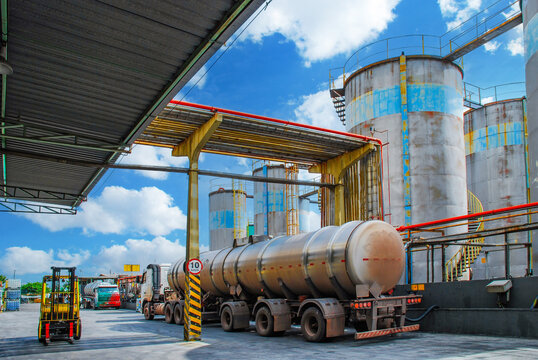 Industrial oil facility featuring large storage tanks, complex pipeline systems, and heavy-duty tanker trucks for fuel distribution and petroleum logistics under a bright blue sky.