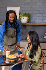 African American barista in denim apron handing coffee cup to Indian customer with phone at cafe © wavebreak3