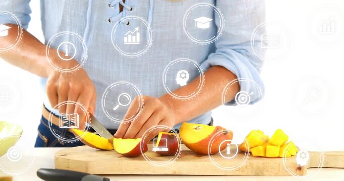 Entering from left cook in light blue blouse, slicing mango on kitchen counter for blender
