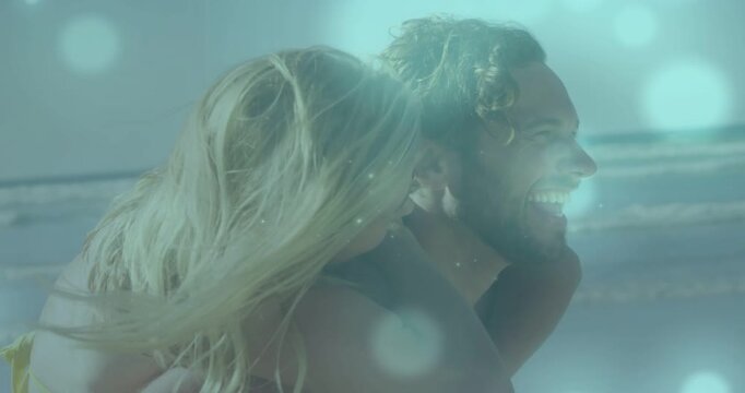 Lifting woman, shirtless man carrying partner in bikini along ocean for fun, lens flare shining